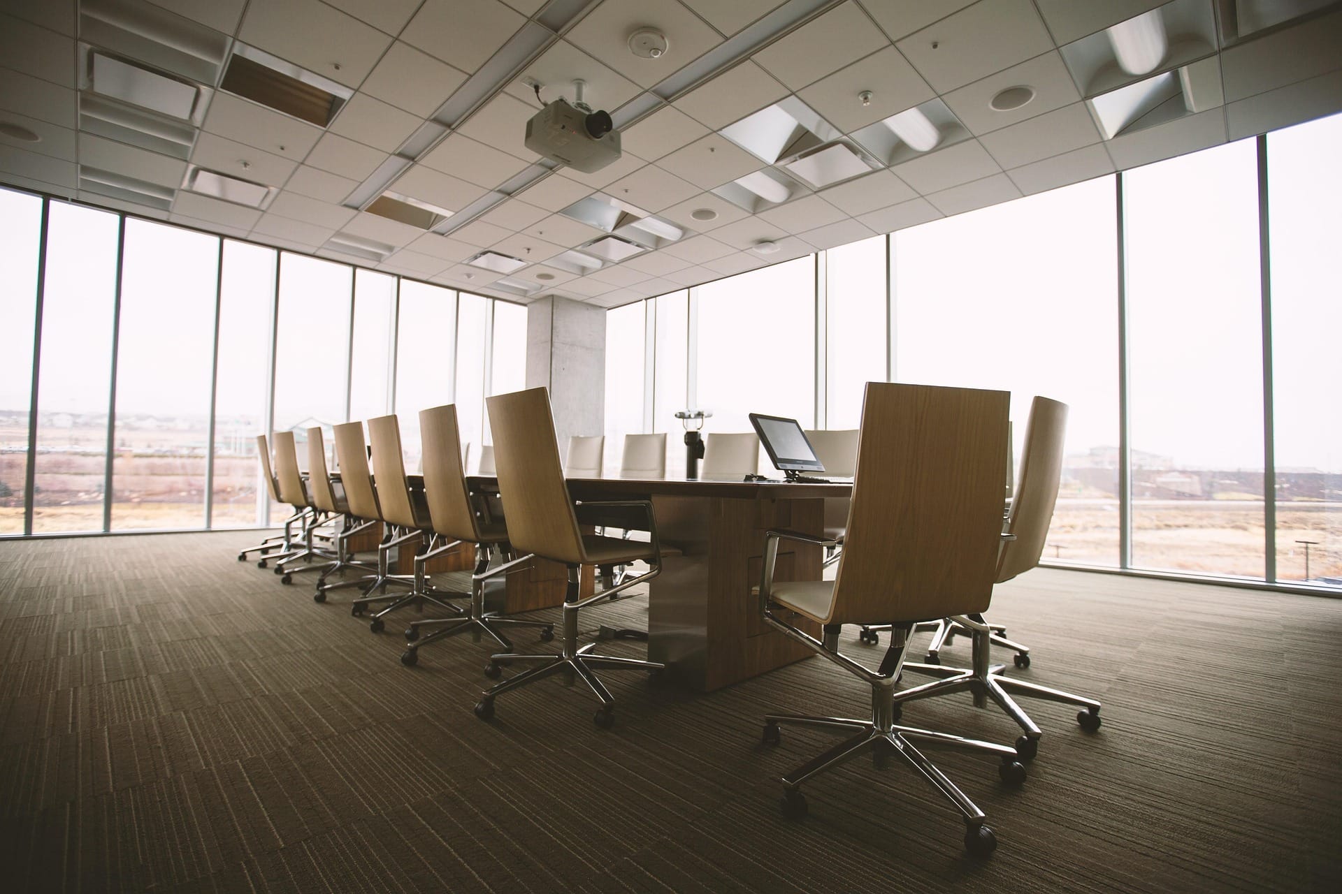 A corporate conference room with long table, roller chairs, and floor to ceiling windows overlooking the grassy landscape